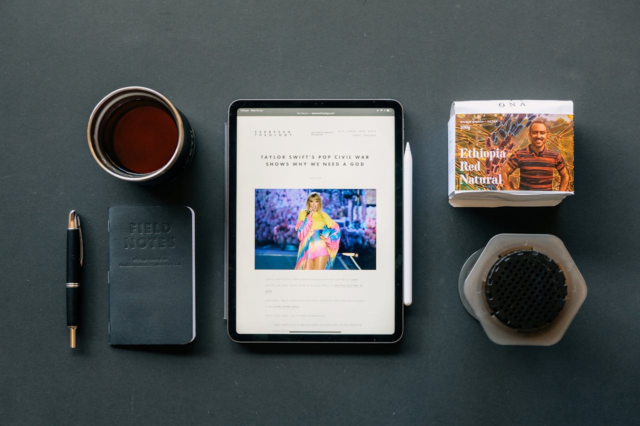 Flat lay of a tablet, coffee, and notebook on a desk, ideal for productivity themes.