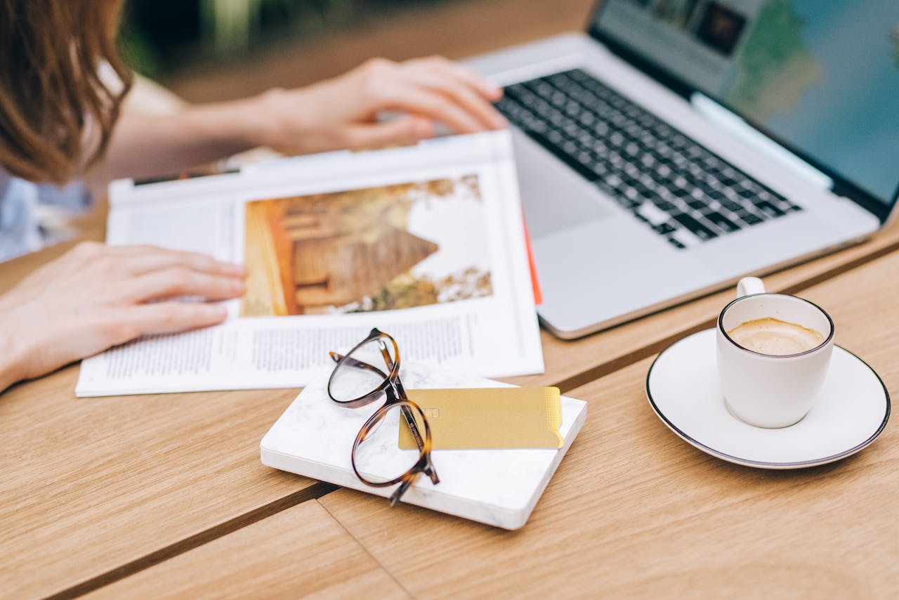 Relaxed desk setup featuring a laptop, coffee, and reading material.